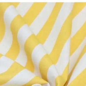 May include: A piece of fabric featuring a repeating pattern of diagonal yellow and white stripes. The material is draped to create soft folds and ripples, highlighting the consistent width of the alternating color bands across the surface.