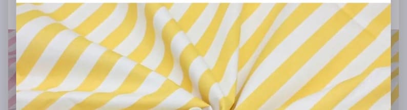 May include: A piece of fabric featuring a repeating pattern of diagonal yellow and white stripes. The material is draped to create soft folds and ripples, highlighting the consistent width of the alternating color bands across the surface.