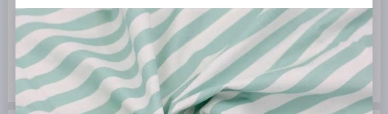 May include: A fabric textile featuring a repeating pattern of diagonal stripes in alternating light mint green and white colors. The material is gathered and folded, creating soft, flowing drapes and shadows across the surface of the cloth.