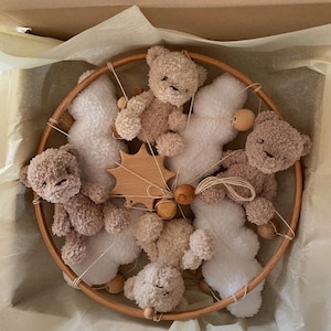 May include: A wooden baby mobile with five plush teddy bears and white cloud shapes. The mobile is suspended from a wooden ring and has wooden beads.