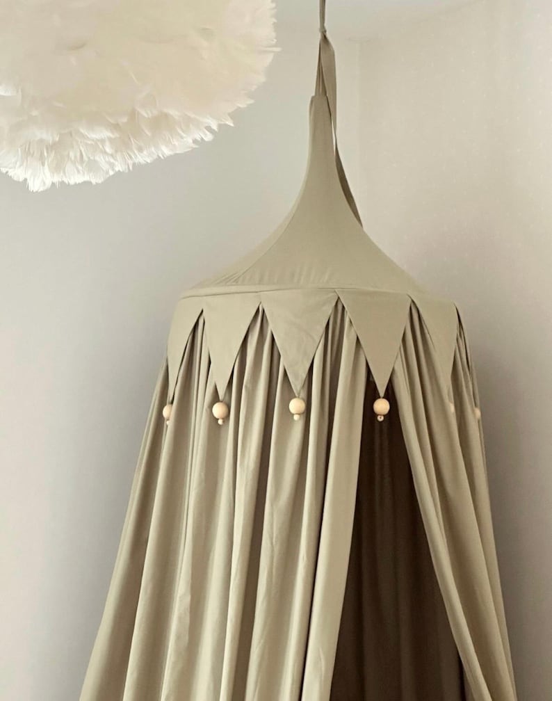 Pu&ograve; includere: Un baldacchino verde salvia con la parte superiore conica e accenti triangolari. Perline di legno pendono dal bordo inferiore. Sullo sfondo &egrave; visibile una nuvola decorativa bianca e soffice. La tenda &egrave; sospesa al soffitto.