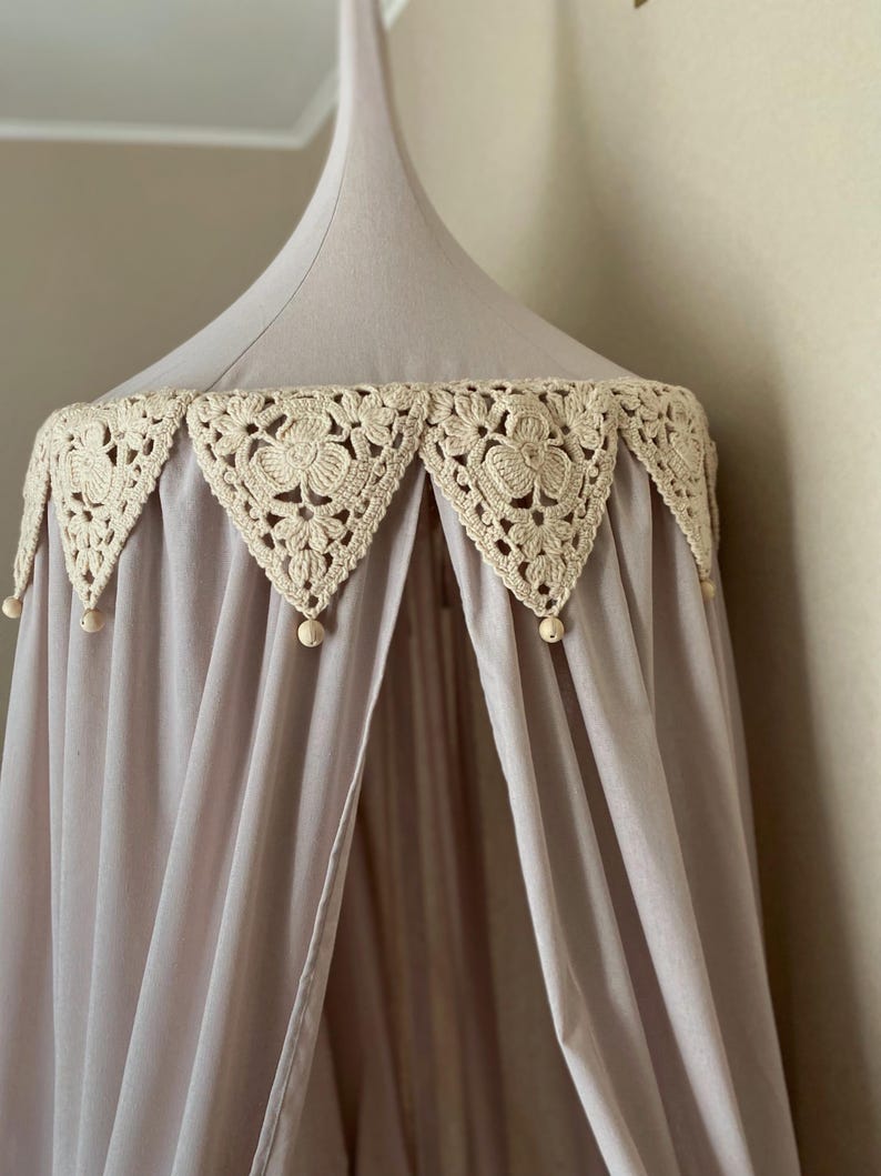 Pu&ograve; includere: Un baldacchino lilla chiaro con un bordo floreale all'uncinetto color crema. Il baldacchino ha una forma conica ed &egrave; realizzato in un tessuto morbido e fluido. Piccole perline di legno pendono dal bordo. Ideale per una cameretta o una camera da letto.
