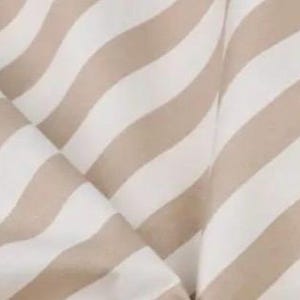 May include: A textile fabric featuring a repeating pattern of diagonal stripes in alternating shades of soft beige and crisp white. The material is draped to create gentle folds and soft curves, highlighting the consistent width of the stripes.