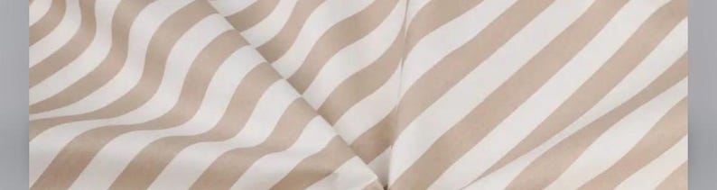 May include: A textile fabric featuring a repeating pattern of diagonal stripes in alternating shades of soft beige and crisp white. The material is draped to create gentle folds and soft curves, highlighting the consistent width of the stripes.