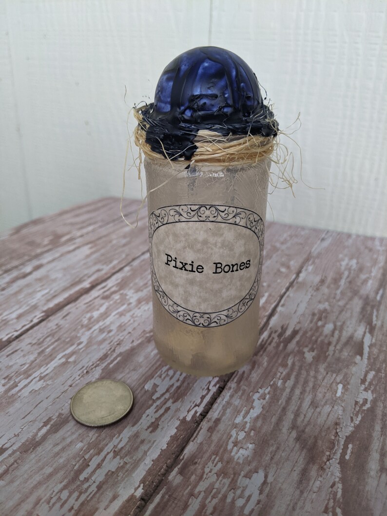May include: A glass jar with a black and blue wax seal, tied with twine, and a label that reads "Pixie Bones".