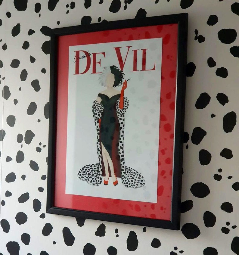Puede incluir: Una impresi&oacute;n enmarcada de Cruella De Vil de la pel&iacute;cula de Disney 101 D&aacute;lmatas. La impresi&oacute;n presenta una ilustraci&oacute;n en blanco y negro de Cruella con un abrigo de estampado d&aacute;lmata rojo y negro, sosteniendo un cigarrillo. La impresi&oacute;n est&aacute; enmarcada en negro con un passe-partout rojo.