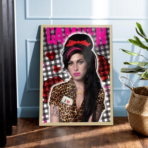 May include: Framed art print featuring a portrait of Amy Winehouse. The image includes the word "CAMDEN" in pink, a black and white checkered background, and red heart and rose accents. The subject wears a leopard print top.