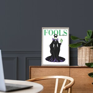 May include: A white framed print with a black and purple illustration of Maleficent from Disney's Sleeping Beauty. The text "FOOLS" is in green letters at the top of the print. The text "They're Amusingly!" is in smaller green letters below the word "FOOLS".