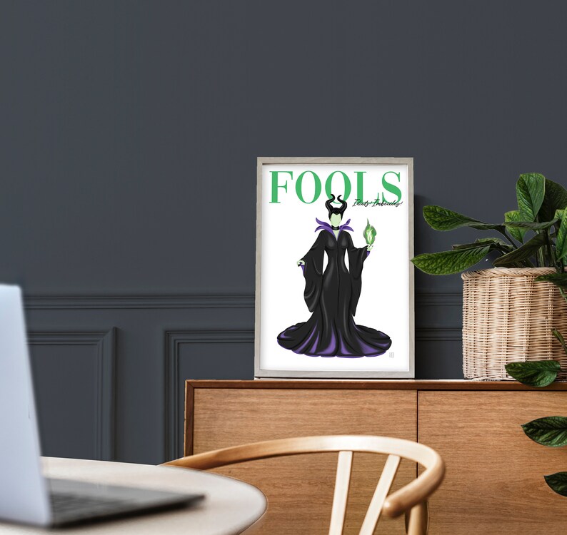 May include: A white framed print with a black and purple illustration of Maleficent from Disney's Sleeping Beauty. The text "FOOLS" is in green letters at the top of the print. The text "They're Amusingly!" is in smaller green letters below the word "FOOLS".