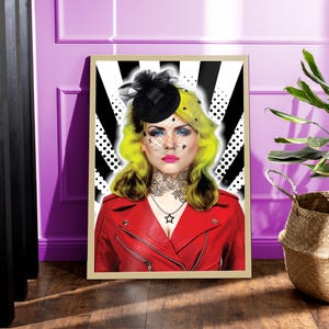 May include: Framed art print of a woman with yellow hair, blue eyes, and a red leather jacket. She wears a black hat with a veil and a star pendant necklace. The background has a black and white design.