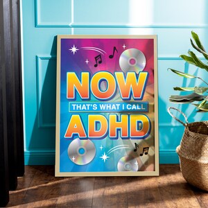 May include: Framed poster with the text "NOW THAT'S WHAT I CALL ADHD" in orange and blue, with CD graphics and musical notes. The poster is in a light brown frame, leaning against a teal wall.