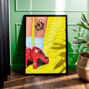 May include: A black framed poster featuring a yellow brick road background. A woman's leg is shown wearing red sparkly shoes and a blue sock. A tattoo of a dog with the text "Somewhere over the rainbow" is on the leg.