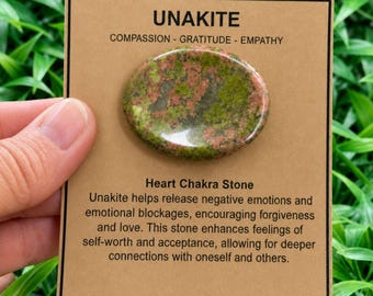 May include: An oval Unakite stone with mottled green and pink patterns mounted on a rectangular tan display card. The card features the text Unakite, Compassion - Gratitude - Empathy, Heart Chakra Stone, and descriptive text about the stone.