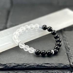 May include: A stretch bracelet featuring a series of round, frosted white beads and polished black beads. The design includes small, silver-toned metal spacer beads encrusted with tiny clear crystals, creating a balanced contrast between the light and dark elements.