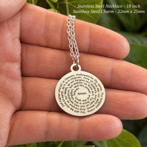 Peut inclure: Un collier en acier inoxydable argent&eacute; avec une cha&icirc;ne de 18 pouces et un pendentif rond de 22 mm x 25 mm. Le pendentif pr&eacute;sente la pri&egrave;re du Notre P&egrave;re grav&eacute;e en noir, en spirale vers le centre avec le mot Amen au milieu du m&eacute;daillon.