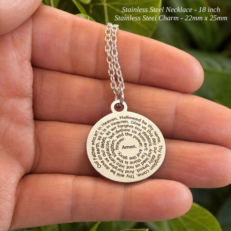 Peut inclure: Un collier en acier inoxydable argent&eacute; avec une cha&icirc;ne de 18 pouces et un pendentif rond de 22 mm x 25 mm. Le pendentif pr&eacute;sente la pri&egrave;re du Notre P&egrave;re grav&eacute;e en noir, en spirale vers le centre avec le mot Amen au milieu du m&eacute;daillon.