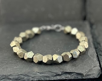May include: A bracelet composed of numerous faceted, metallic gold-toned pyrite beads. The beads are irregularly shaped with multiple flat surfaces, creating a textured appearance. The bracelet features a small, silver-toned metal clasp closure.
