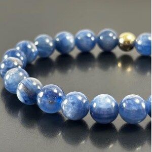 Peut inclure: Un bracelet de perles composé de pierres précieuses de cyanite bleu profond, rondes et lisses, présentant des variations de couleur naturelles et une perle métallique dorée polie. Les perles sont disposées en cercle avec une finition brillante.