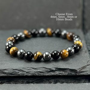 May include: A bracelet made of black, tiger's eye, and silver-coloured beads. The bracelet is presented on a dark grey surface. Text on the image reads: Choose From 4mm, 6mm, 8mm or 10mm Beads.