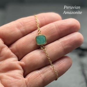 May include: A delicate gold chain bracelet featuring a single square-cut Peruvian Amazonite gemstone in a gold setting. The stone is a soft, opaque teal-green colour. The text "Peruvian Amazonite" is visible in the upper right corner of the image.