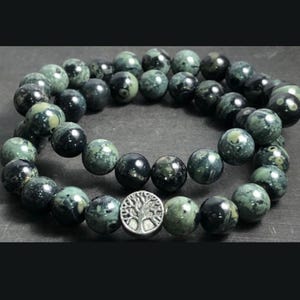 May include: A double-strand bracelet made of dark green and black speckled beads with a silver tree of life charm.