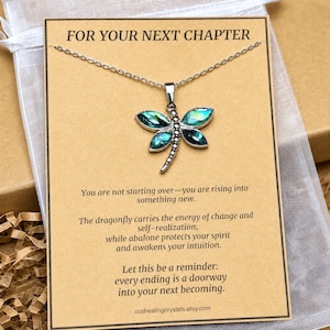 May include: A silver-toned dragonfly pendant necklace featuring iridescent abalone shell wings. The pendant is displayed on a tan card with the text FOR YOUR NEXT CHAPTER and a message about change, self-realisation, and intuition.
