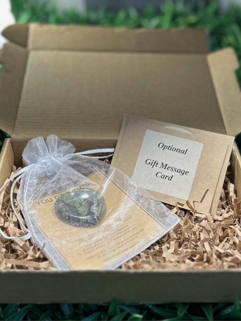 May include: A brown cardboard gift box filled with shredded paper, containing a small green stone heart inside a white organza drawstring pouch, and a tan card labeled Optional Gift Message Card with printed text.
