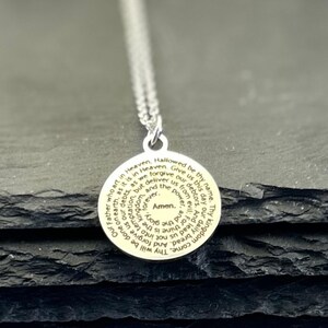 Peut inclure: Un pendentif circulaire argent&eacute; avec la pri&egrave;re du Notre P&egrave;re grav&eacute;e en noir, formant une spirale vers le centre o&ugrave; est inscrit le mot Amen. Le pendentif est suspendu &agrave; une fine cha&icirc;ne &agrave; maillons de couleur argent&eacute;e.