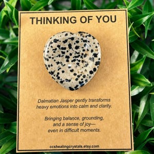 May include: A heart-shaped Dalmatian Jasper stone with black spots on a cream background, mounted on a rectangular tan card. The card features the text THINKING OF YOU, followed by a description of the stone and the website ccshealingcrystals.etsy.com.