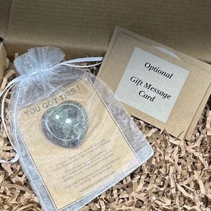 May include: A heart-shaped green stone inside a white organza drawstring bag, placed on a card with the text YOU GOT THIS! and a description of Dragon's Blood stone, alongside a separate card labeled Optional Gift Message Card.