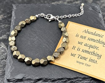 May include: A bracelet made of faceted metallic pyrite beads with a silver-toned metal chain and lobster clasp. A tan card is included with the printed text: Abundance is not something we acquire. It is something we Tune into. Wayne Dyer.
