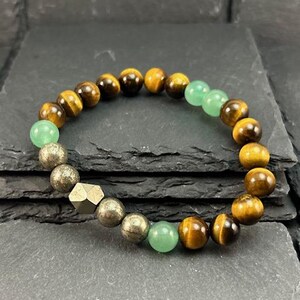 May include: A beaded bracelet featuring round tiger eye beads in shades of brown and gold, interspersed with smooth light green aventurine beads and metallic pyrite beads, including one faceted geometric pyrite bead in the center.