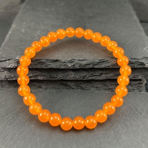 May include: A circular stretch bracelet composed of numerous smooth, round, vibrant orange beads. The beads are uniform in size and shape, creating a continuous loop that forms the bracelet. The orange color is consistent across all beads.