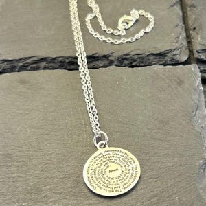 Peut inclure: Un collier argent&eacute; dot&eacute; d'un pendentif circulaire grav&eacute; du texte de la pri&egrave;re du Notre P&egrave;re en noir. Le pendentif est fix&eacute; &agrave; une fine cha&icirc;ne argent&eacute;e avec un fermoir mousqueton, formant un bijou simple et &eacute;l&eacute;gant pour le quotidien.