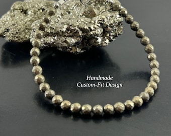 May include: A bracelet made of small, faceted, metallic gold-toned pyrite beads with a silver-toned lobster claw clasp. The text "Handmade Custom-Fit Design" is printed in white in the centre of the circular arrangement of the beads.