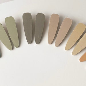 May include: A set of 10 hair clips in various shades of beige, brown, and blue. The clips are arranged in a semi-circle, with the lightest shades at the top and the darkest shades at the bottom.