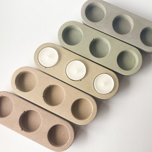 May include: Five rectangular concrete candle holders with three candle wells each. The holders are arranged in a gradient from light green to beige.