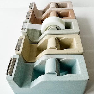 K&ouml;nnte beinhalten: Vier Klebebandspender in verschiedenen Farben: hellblau, beige, hellbraun und braun. Die Spender sind aus Beton und haben einen Vintage-Look.