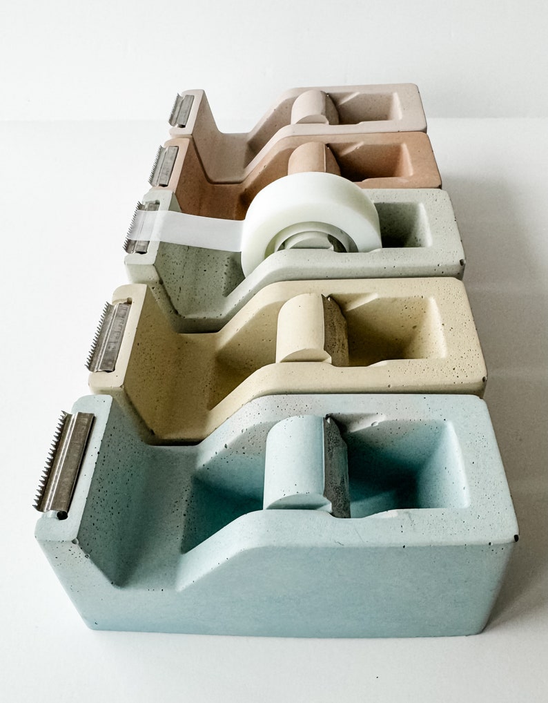 K&ouml;nnte beinhalten: Vier Klebebandspender in verschiedenen Farben: hellblau, beige, hellbraun und braun. Die Spender sind aus Beton und haben einen Vintage-Look.