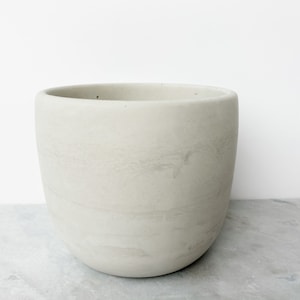 May include: A light gray, round, ceramic planter with a smooth, slightly textured surface.