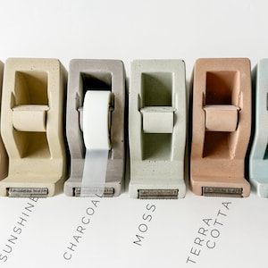 K&ouml;nnte beinhalten: Sechs Beton-Klebebandspender in verschiedenen Farben: Blush, Sonnenschein, Anthrazit, Moos, Terrakotta und Himmel. Jeder Spender hat eine andere Klebebandrolle, darunter transparentes Klebeband, gemustertes Klebeband und Washi-Tape.