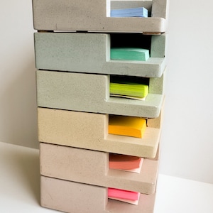 May include: A stacked concrete desk organizer with six compartments, each holding a stack of colorful sticky notes. The organizer is in shades of gray and beige, with blue, green, yellow, orange, and pink notes.