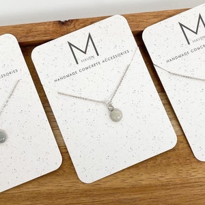May include: Three white cards with a silver chain necklace with a small round pendant on each. The cards have the text "MAVEN HANDMADE CONCRETE ACCESSORIES" on them.
