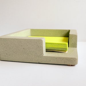 May include: A light green concrete desk organizer with a stepped design. The organizer holds a stack of bright yellow sticky notes. The desk accessory has a modern, minimalist aesthetic and is suitable for home or office use.