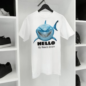May include: White t-shirt featuring a blue shark graphic and the text "HELLO My Name's Bruce".