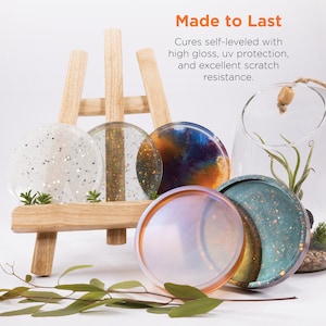 May include: Five round resin coasters in various colors and patterns, including white with glitter, gold glitter, blue and orange swirl, iridescent, and teal with glitter. The coasters are displayed on a wooden easel. "Made to Last" is written in orange text above the coasters. The text below reads "Cures self-leveled with high gloss, uv protection, and excellent scratch resistance."