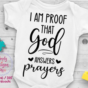 May include: White baby onesie with black text that reads "I am proof that God answers prayers". There are two small hearts above the word "answers".