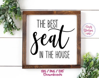 Könnte beinhalten: Ein Holzschild mit dem Text "THE BEST seat IN THE HOUSE" in schwarzen Buchstaben. Das Schild befindet sich auf einem weißen Hintergrund mit grünen Pflanzen auf beiden Seiten.