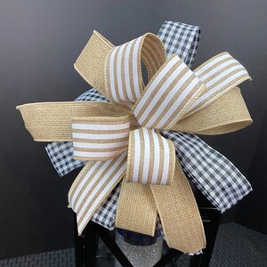 May include: A black metal lantern with a glass insert and a decorative bow made of burlap, white and brown striped ribbon, and black and white gingham ribbon.