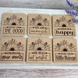 May include: Six square cork coasters with inspirational quotes and floral designs. Each coaster features a different phrase: "Focus on the Good," "You are enough," "Choose happy," "Remember your worth," "Be real, not perfect," and "Enjoy the little things."